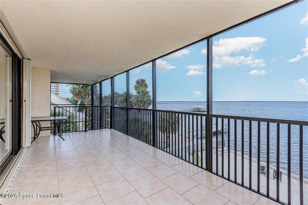 A screened-in balcony with tile flooring overlooks a body of water and a pier — 525 INDIAN RIVER AVENUE UNIT 303, TITUSVILLE, FL