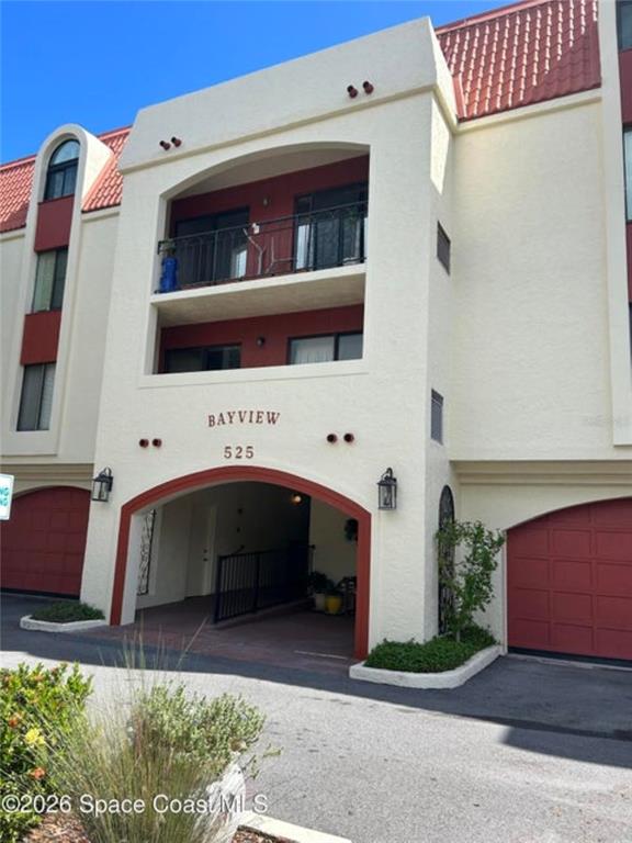The exterior of a multi-story building features a covered entrance, a balcony, and red garage doors — 525 INDIAN RIVER AVENUE UNIT 303, TITUSVILLE, FL