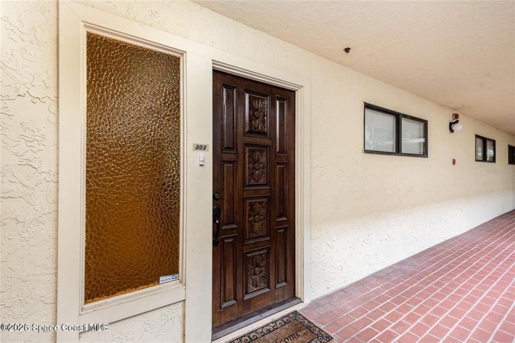 An exterior view shows a brown wooden door with floral carvings next to a window — 525 INDIAN RIVER AVENUE UNIT 303, TITUSVILLE, FL