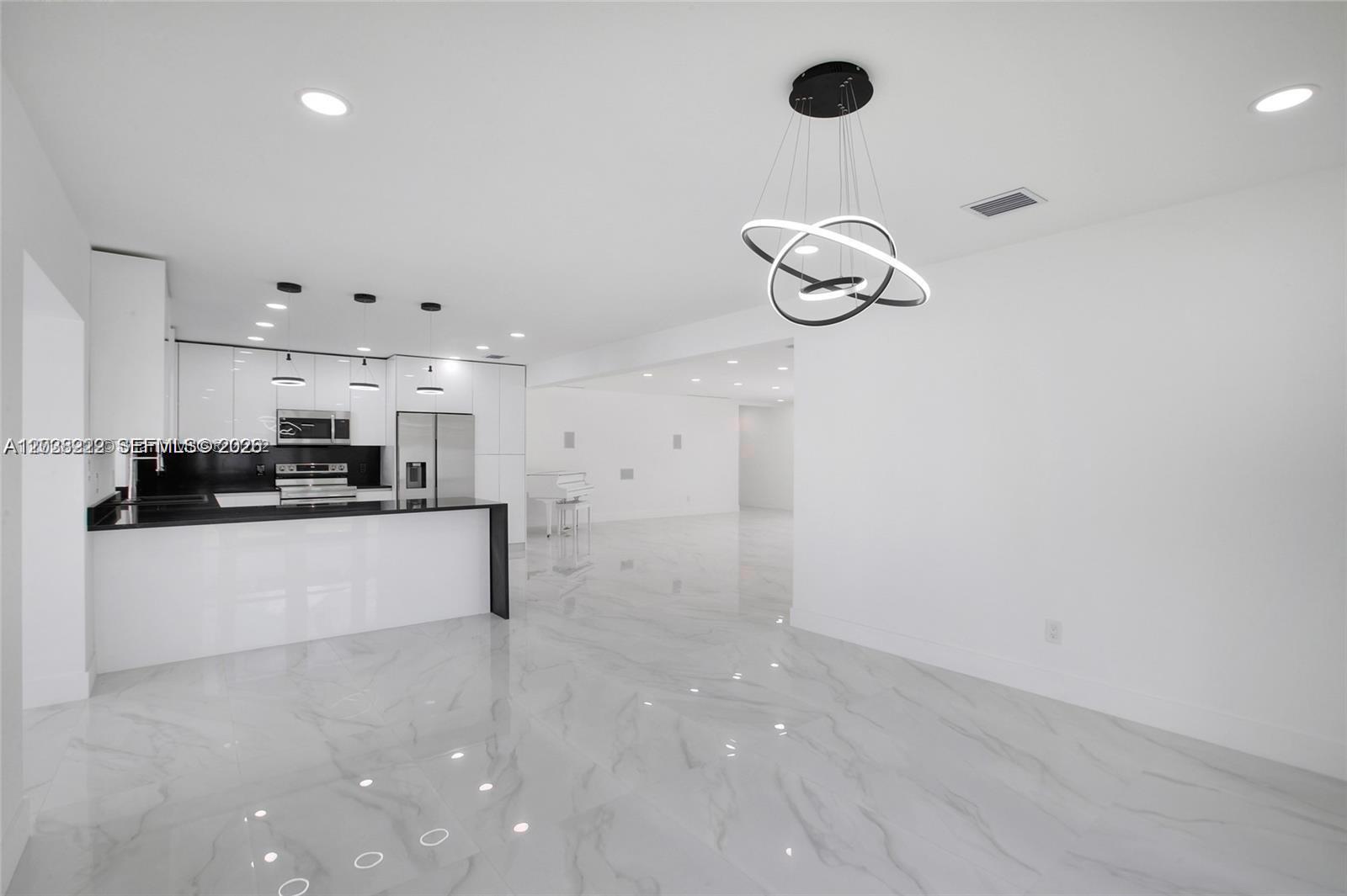 A modern kitchen with black countertops and white cabinets opens into a spacious living area — 1825 NE 197th Ter, Miami FL 33179, MIAMI, FL