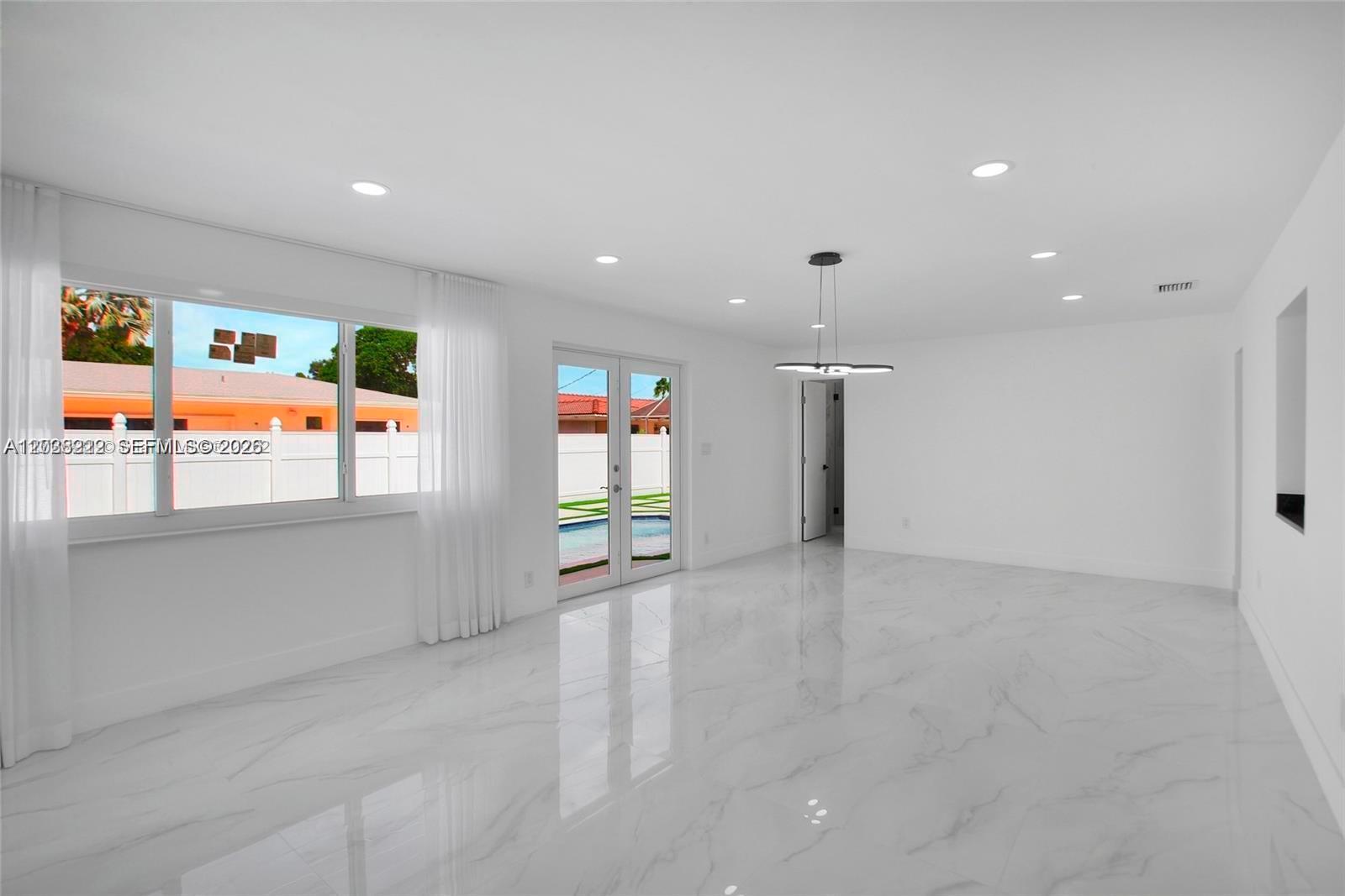 A bright, empty room features white marble-look tile flooring, recessed lighting, and glass patio doors — 1825 NE 197th Ter, Miami FL 33179, MIAMI, FL