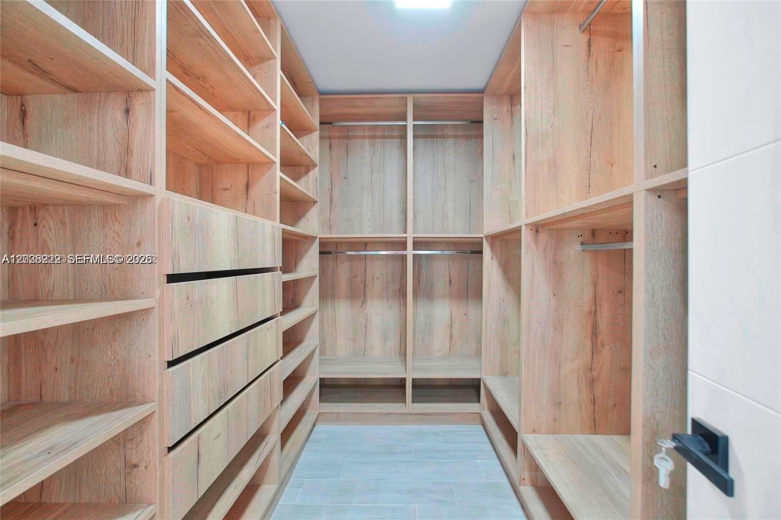 A walk-in closet features light wood shelving, hanging rods, and drawers with tiled flooring — 1825 NE 197th Ter, Miami FL 33179, MIAMI, FL