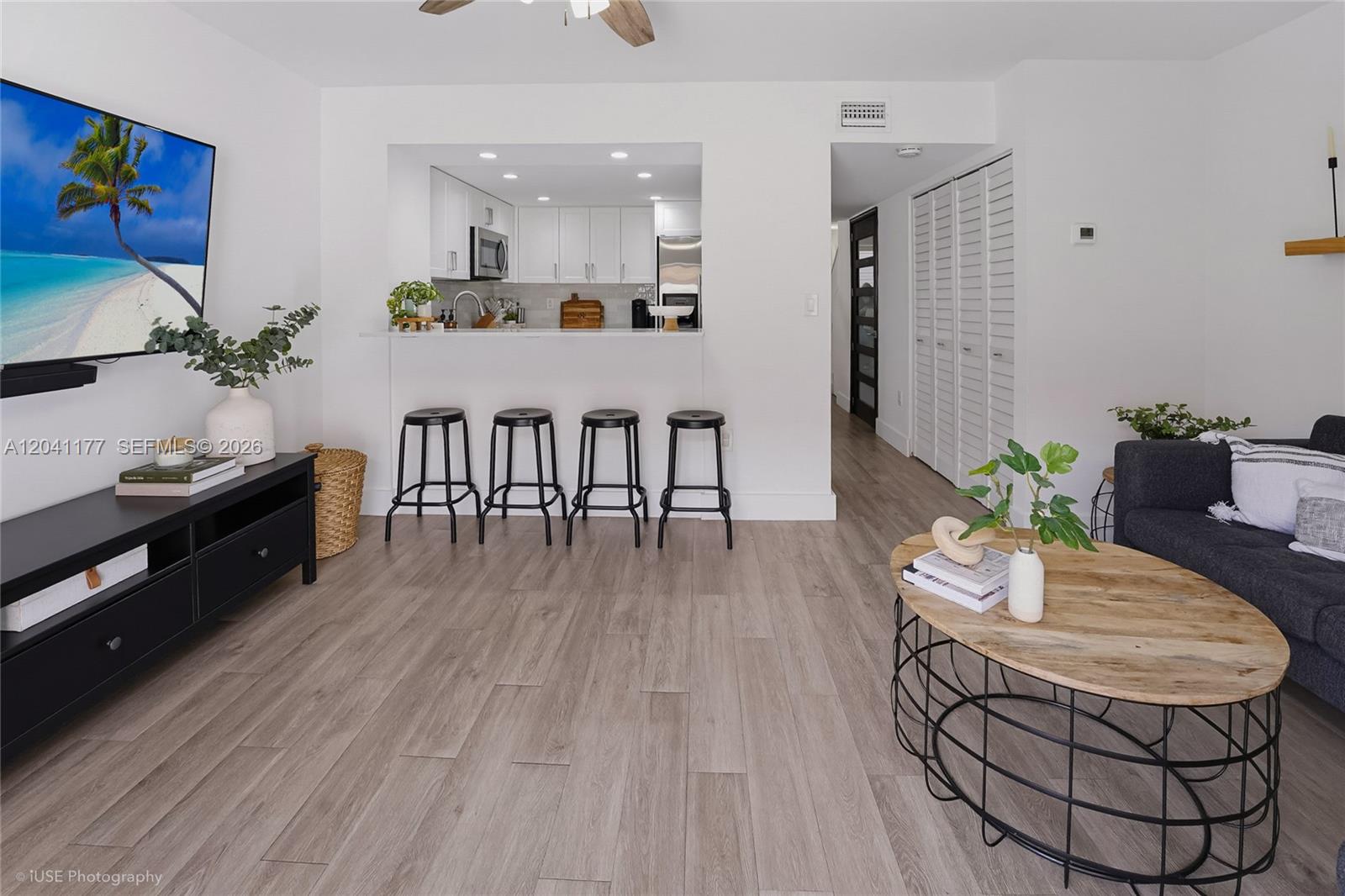 A living room features light wood-look flooring, a kitchen pass-through with bar stools, and a television — 10137 SW 77th Ct, Miami FL 33156, MIAMI, FL