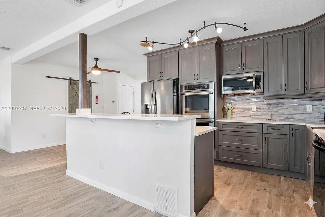 A kitchen features gray cabinets, stainless steel appliances, and a white peninsula countertop — 316 NW 29th St, Wilton Manors FL 33311, WILTON MANORS, FL