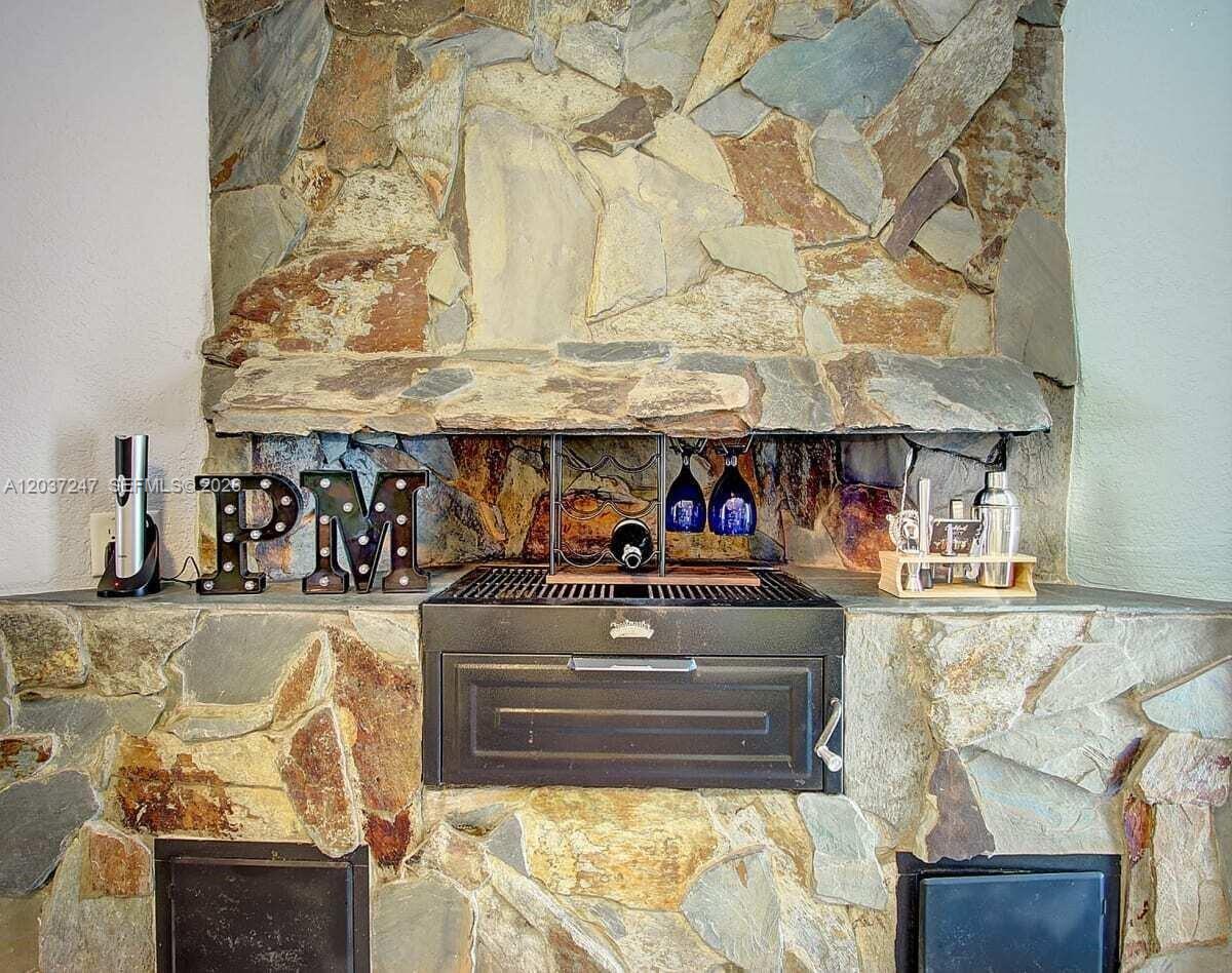 A stone fireplace features a built-in grill, decorative letters, and bar accessories on the hearth — 316 NW 29th St, Wilton Manors FL 33311, WILTON MANORS, FL