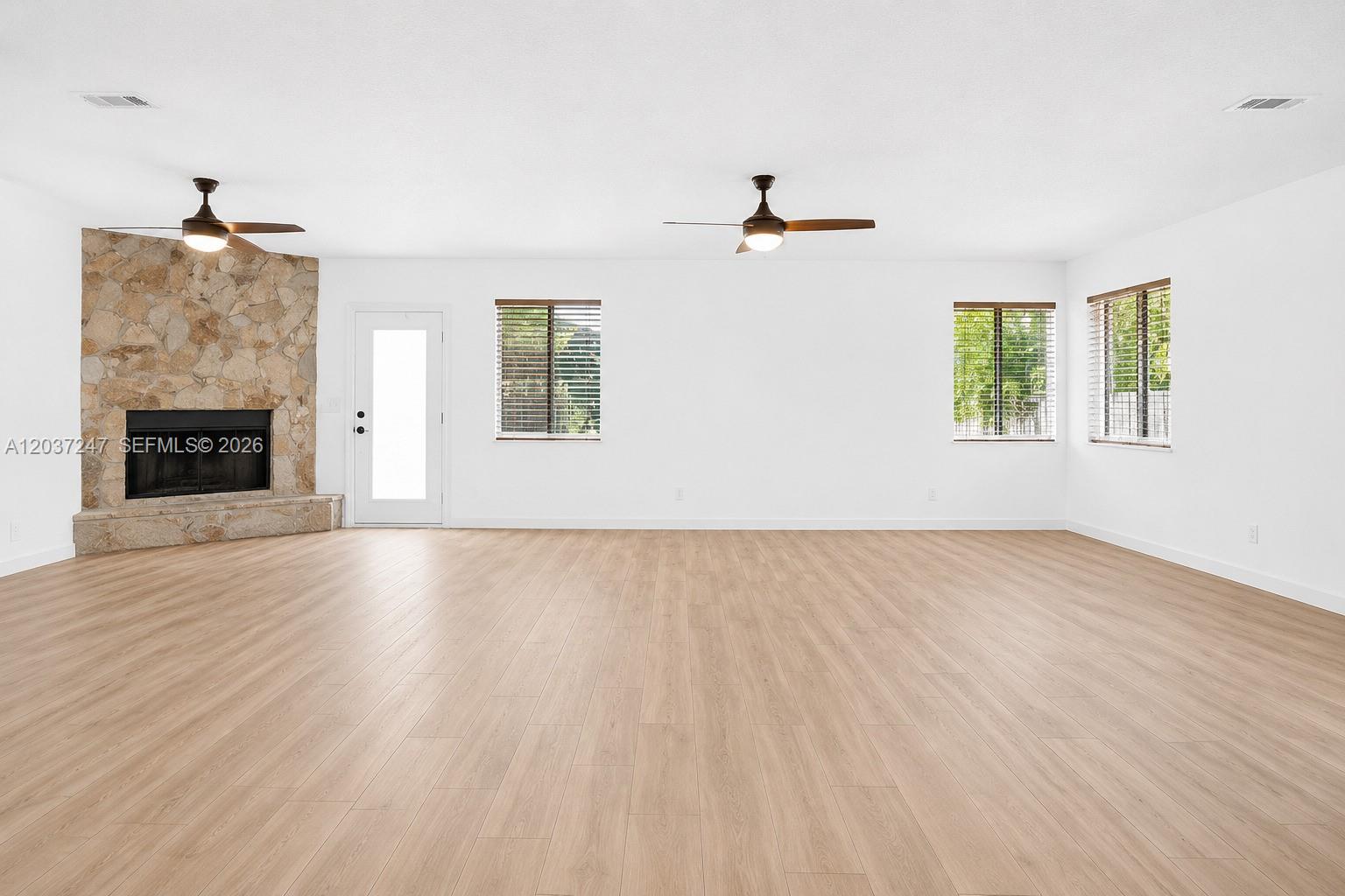 A spacious living room features light wood-look flooring, white walls, and a stone fireplace — 316 NW 29th St, Wilton Manors FL 33311, WILTON MANORS, FL
