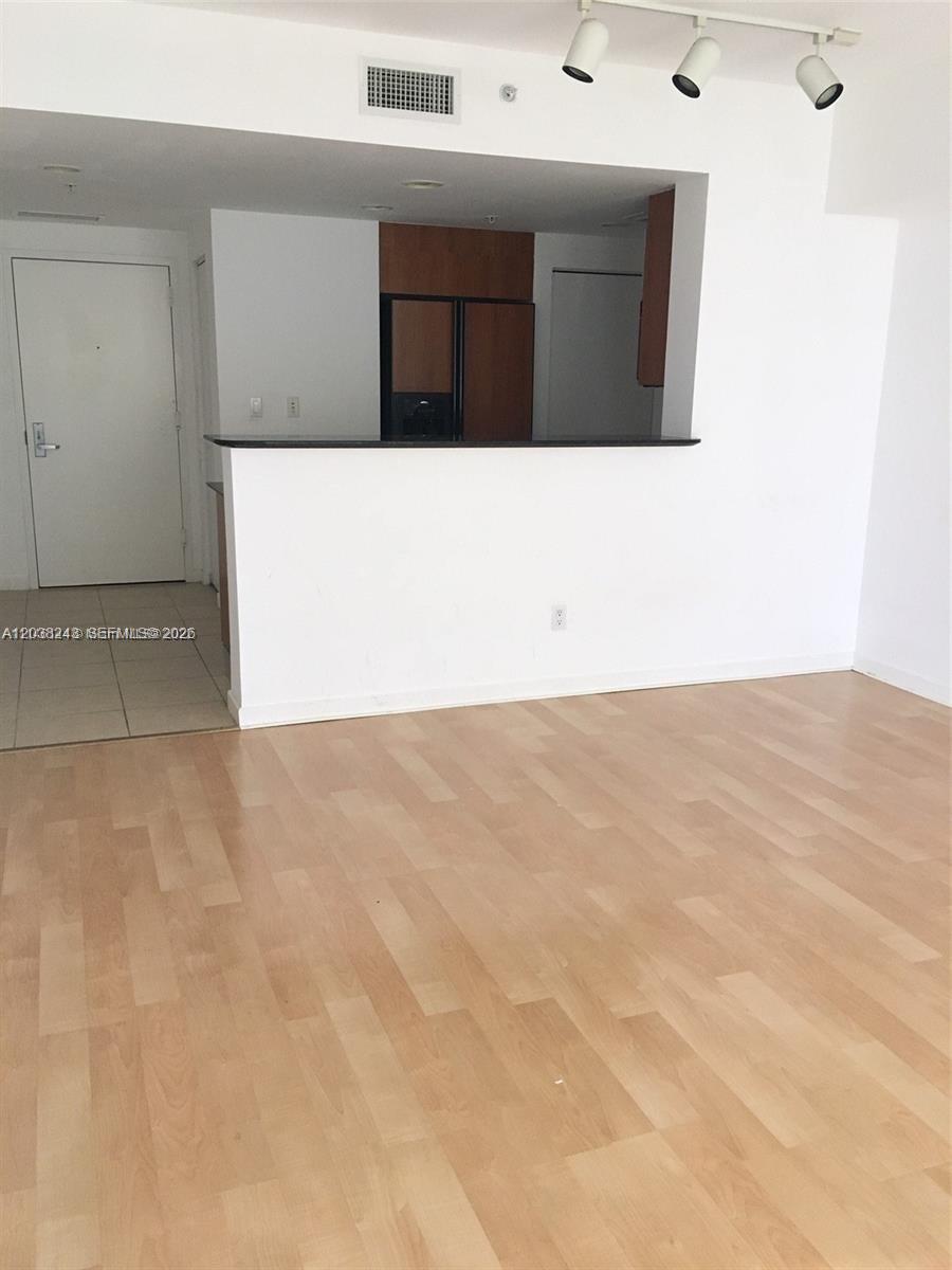 A living room with light wood flooring looks toward a kitchen with a breakfast bar — 335 S Biscayne Blvd # 2006, Miami FL 33131, MIAMI, FL
