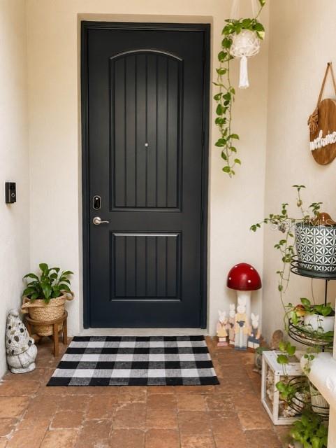 A dark front door with a buffalo check rug sits on a brick porch — 1194 PAISLEY COURT, LAKE WORTH, FL
