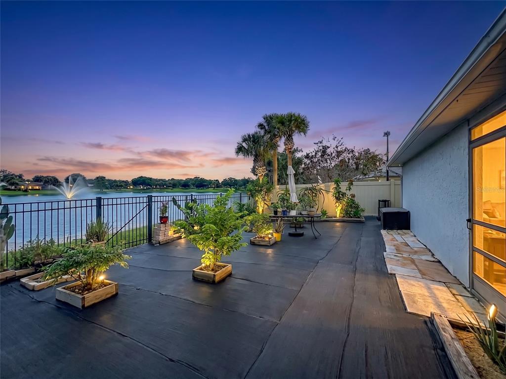 A patio with a black ground cover, potted plants, and a metal fence overlooking a lake — 2405 SETTLERS TRAIL, ORLANDO, FL