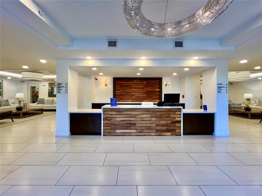 A modern lobby features a wood-paneled reception desk, white tile flooring, and a large chandelier — 16300 COUNTY ROAD 455 UNIT 513, MONTVERDE, FL