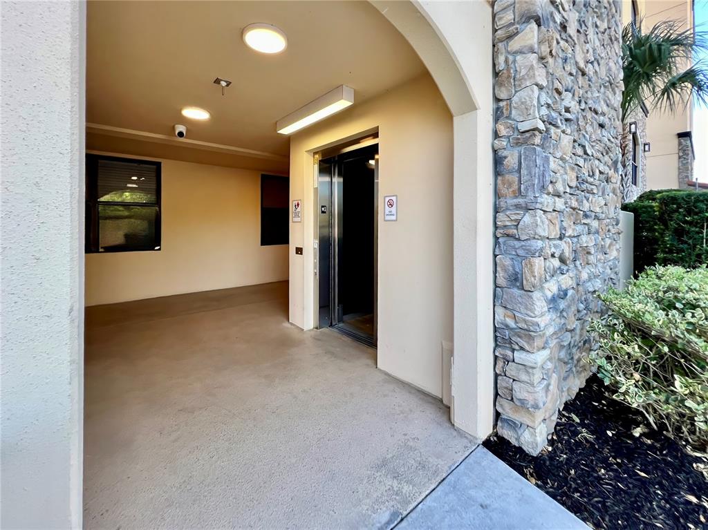 An outdoor elevator entrance features a stone-clad exterior wall and a covered concrete walkway — 16300 COUNTY ROAD 455 UNIT 513, MONTVERDE, FL