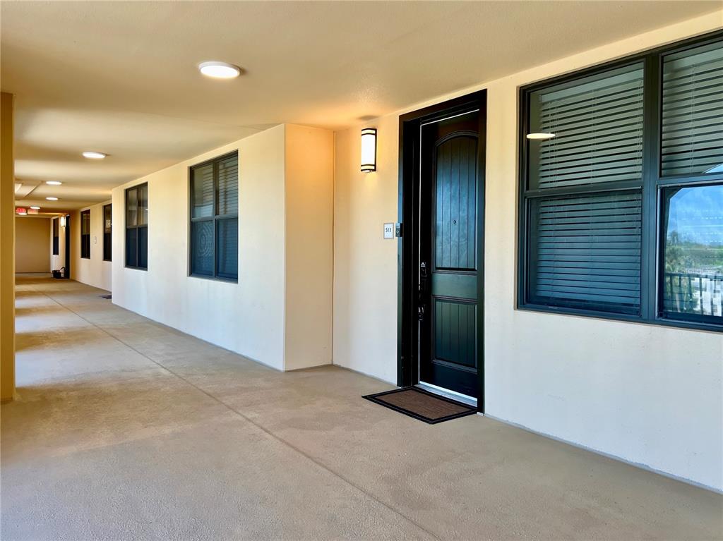 A dark-colored door with a small mat sits along a concrete outdoor apartment hallway — 16300 COUNTY ROAD 455 UNIT 513, MONTVERDE, FL