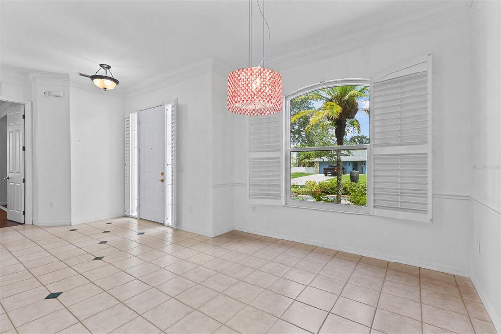 A bright dining room with white walls, tiled floors, a pink chandelier, and arched window — 3732 COUNTRYSIDE ROAD, SARASOTA, FL