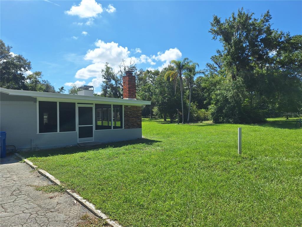 A gray house with a brick chimney and a screened porch sits on a grassy lot — 7606 VAN DYKE ROAD, ODESSA, FL