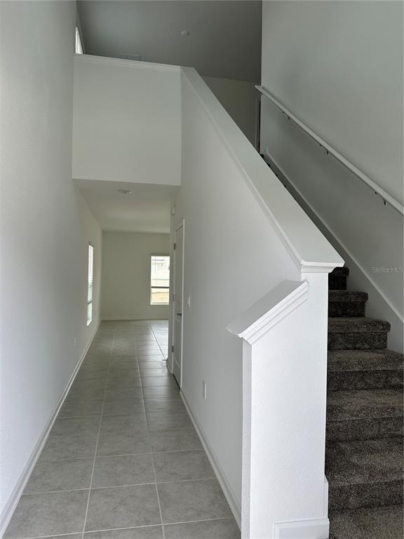 A tiled hallway leads past a carpeted staircase with a white railing — 26277 FEATHERGRASS CIRCLE, LEESBURG, FL