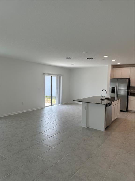 An open-concept kitchen with a granite island and tile flooring leads to a sliding door — 26277 FEATHERGRASS CIRCLE, LEESBURG, FL