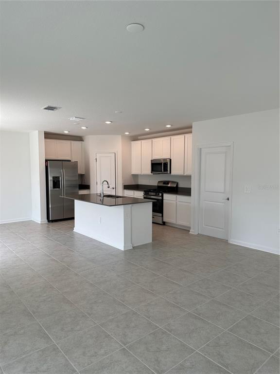 A kitchen features white cabinets, stainless steel appliances, a center island, and tiled flooring — 26277 FEATHERGRASS CIRCLE, LEESBURG, FL