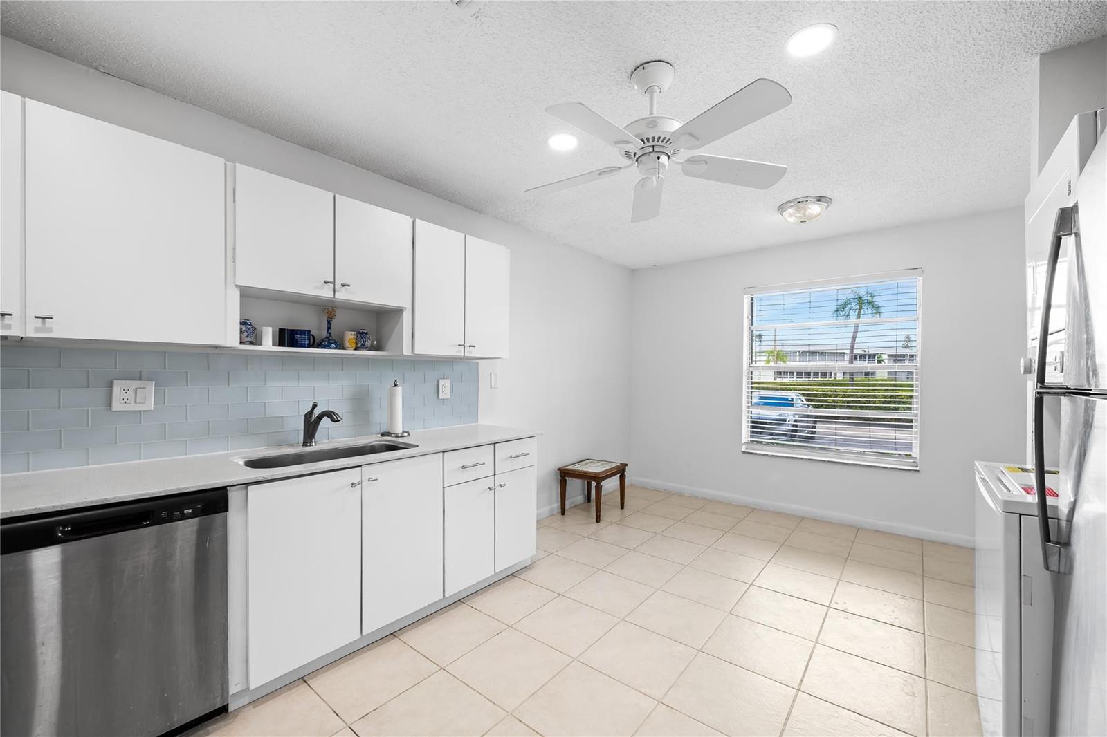 A kitchen with white cabinets, a light blue backsplash, stainless steel appliances, and tile flooring — 1840 NW 13th Street # 103, Delray Beach FL 33445, DELRAY BEACH, FL