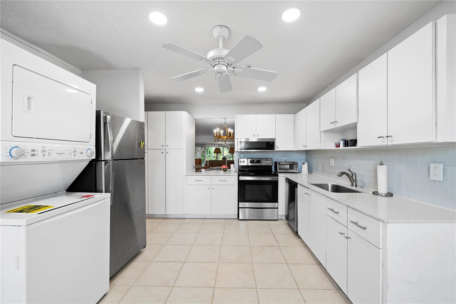 A kitchen features white cabinets, stainless steel appliances, a stacked washer-dryer, and light tile flooring — 1840 NW 13th Street # 103, Delray Beach FL 33445, DELRAY BEACH, FL