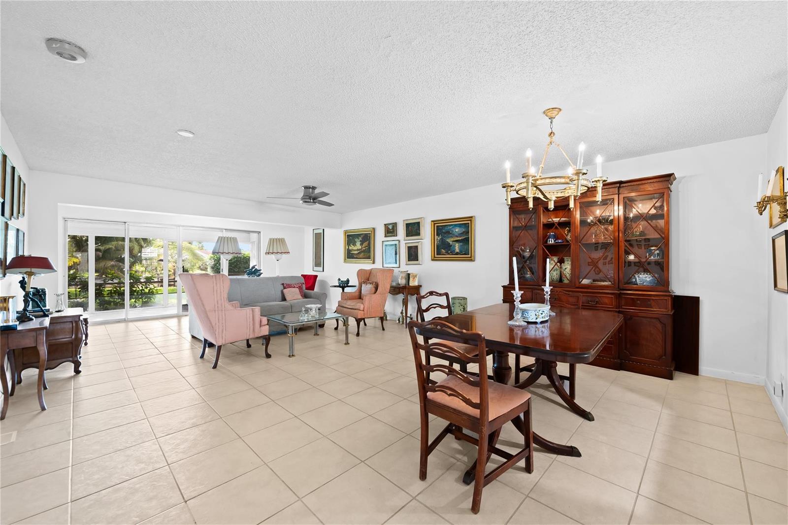 A spacious living and dining area features tile flooring, a wooden hutch, and sliding glass doors — 1840 NW 13th Street # 103, Delray Beach FL 33445, DELRAY BEACH, FL