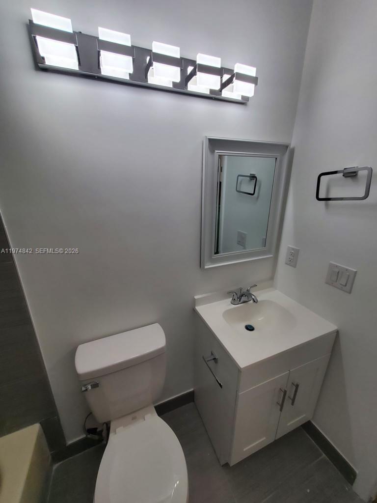 A bathroom features a white vanity, a toilet, a wall-mounted mirror, and a light fixture — NORTH LAUDERDALE, FL