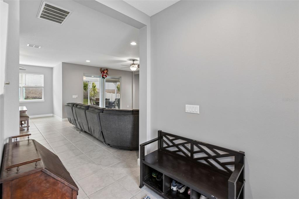 A hallway with a shoe bench leads into an open-concept living room with tile floors — 1084 CAVENDER CREEK ROAD, MINNEOLA, FL