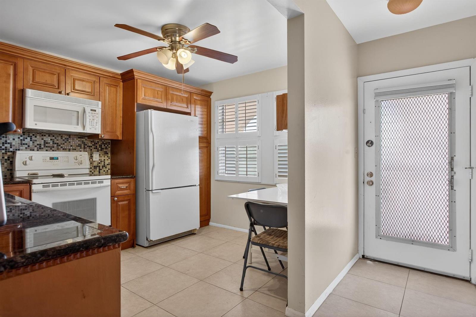 A kitchen features wood cabinets, a white refrigerator, a tile floor, and a dining area — 2003 Granada Drive # L4, Coconut Creek FL 33066, COCONUT CREEK, FL
