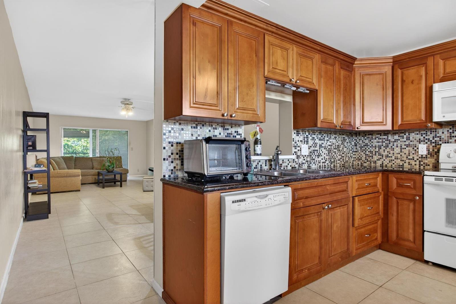 A kitchen with wood cabinets and a mosaic tile backsplash opens into a living room — 2003 Granada Drive # L4, Coconut Creek FL 33066, COCONUT CREEK, FL