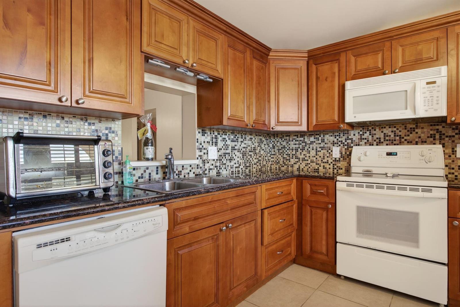 A kitchen with wood cabinets, mosaic tile backsplash, granite countertops, and white appliances — 2003 Granada Drive # L4, Coconut Creek FL 33066, COCONUT CREEK, FL