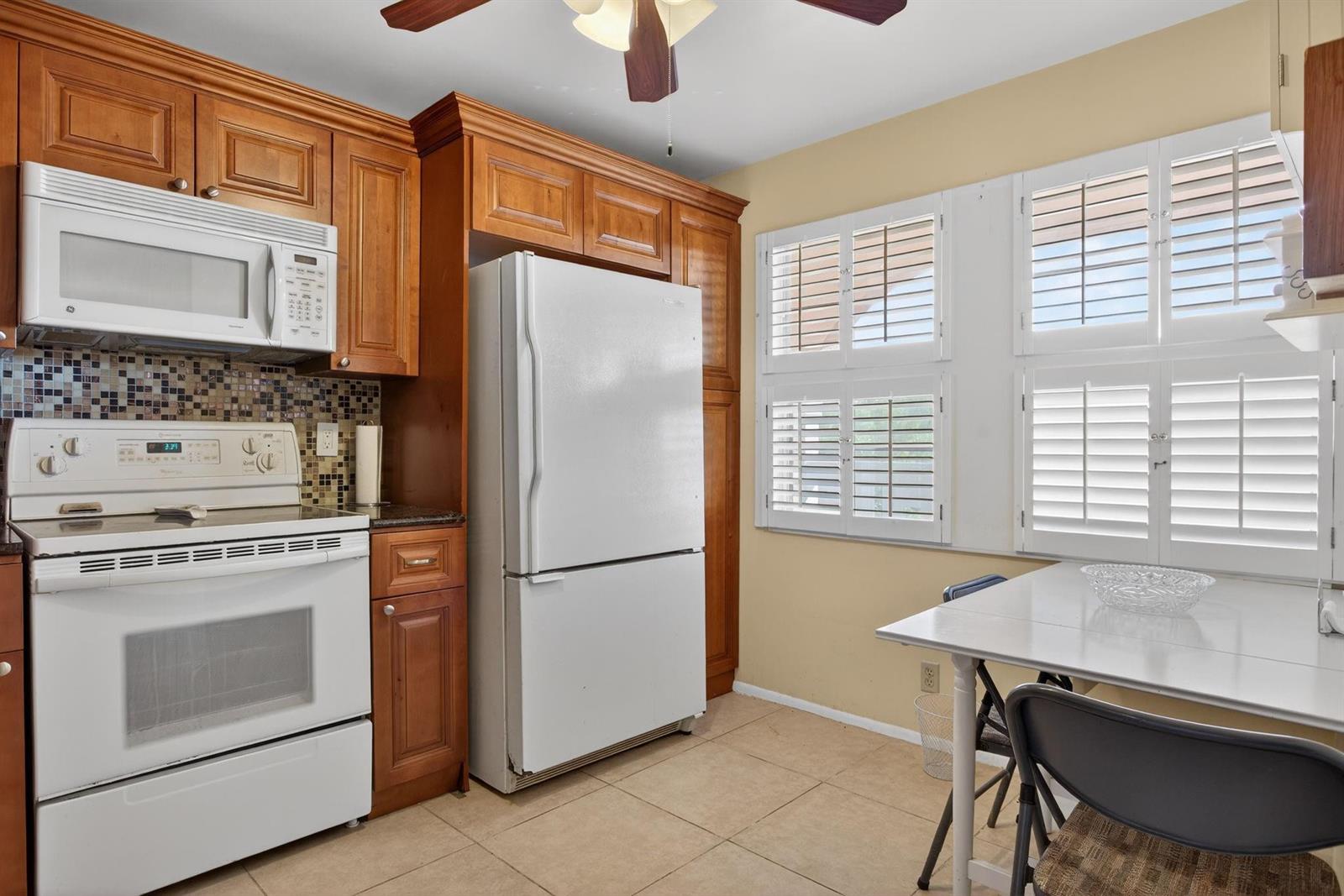 A kitchen features wooden cabinets, white appliances, a tiled backsplash, and a small dining table — 2003 Granada Drive # L4, Coconut Creek FL 33066, COCONUT CREEK, FL