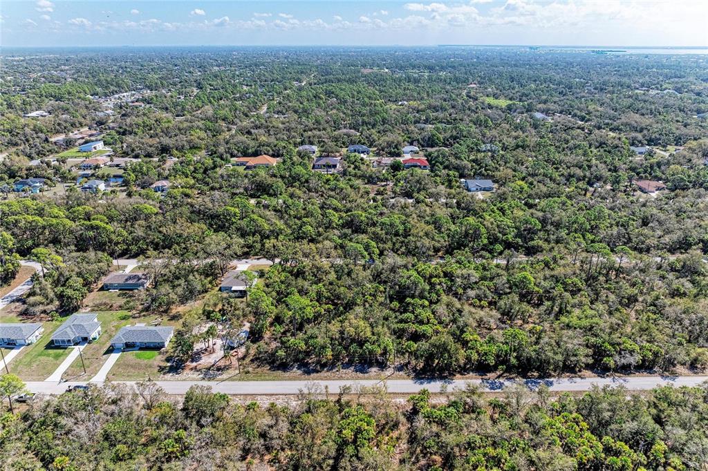 An aerial view shows a residential street with scattered houses surrounded by dense wooded areas — 3115 COMO STREET, PORT CHARLOTTE, FL