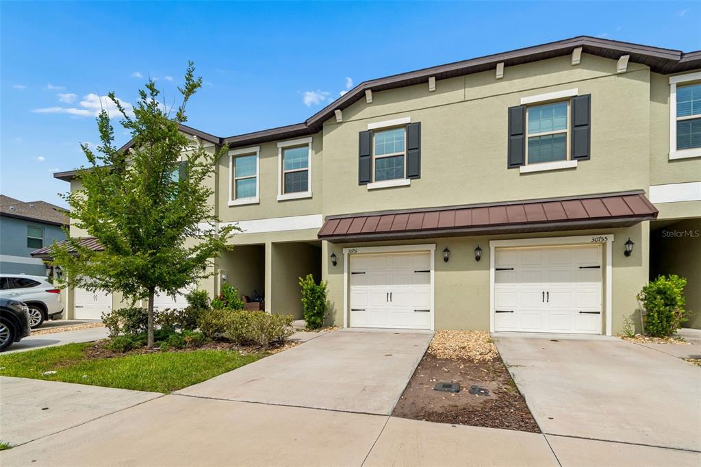 A two-story townhouse exterior features light green stucco walls, two white garage doors, and windows — 30751 VERIDIAN WAY, WESLEY CHAPEL, FL