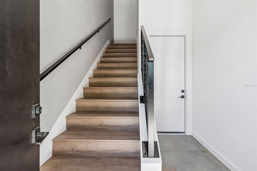A staircase with wood-look steps and a metal railing leads upward next to a door — 1218 E KAY STREET UNIT 21, TAMPA, FL