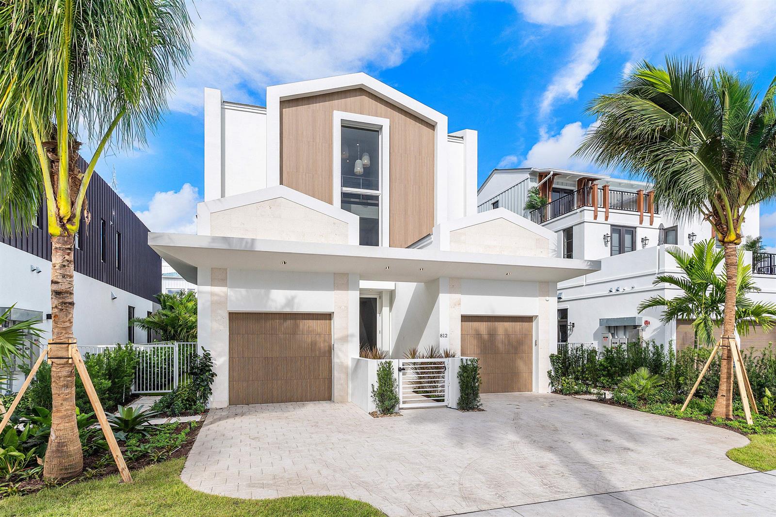 A modern two-story house features a white facade, wood-toned garage doors, and two palm trees — 812 Palm Trail, Delray Beach FL 33483, DELRAY BEACH, FL