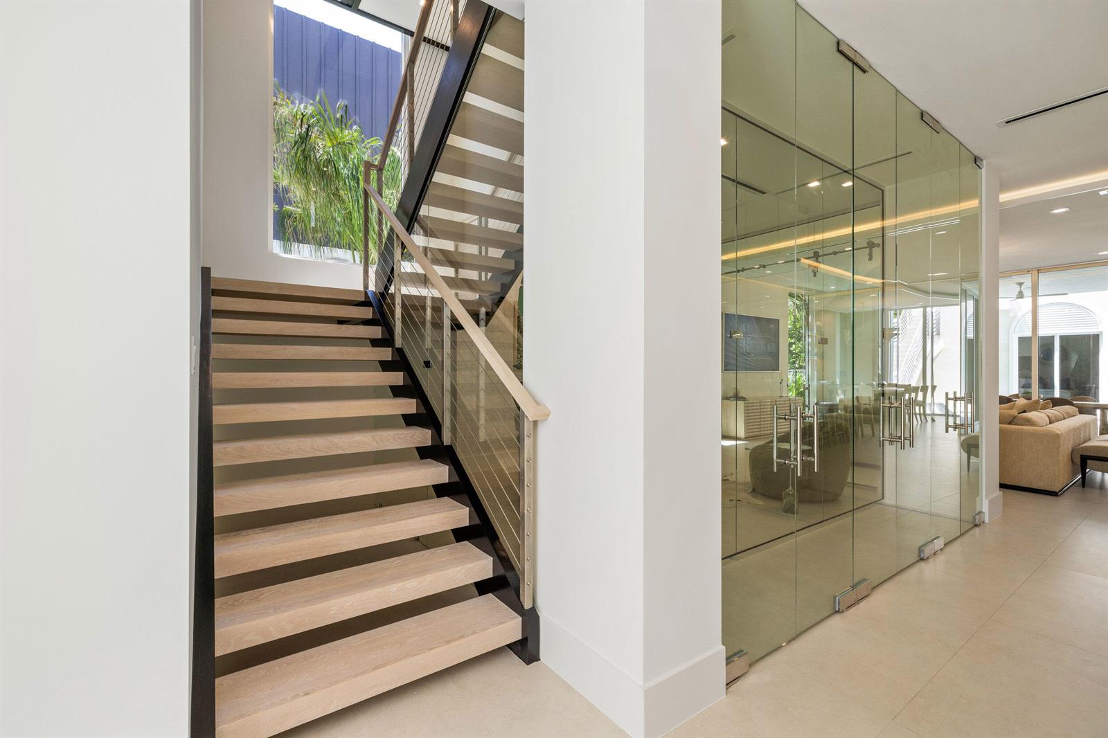 A modern staircase with light wood treads sits beside a glass-enclosed room in a bright hallway — 812 Palm Trail, Delray Beach FL 33483, DELRAY BEACH, FL