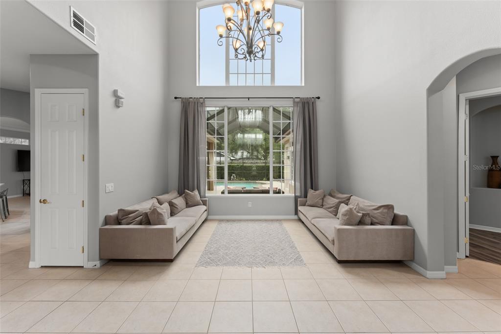 A high-ceilinged living room features two beige sofas, a central rug, and large windows — 14411 HAMPSHIRE BAY CIRCLE, WINTER GARDEN, FL
