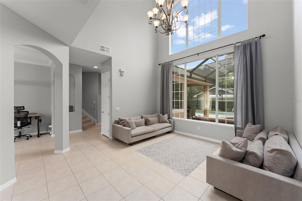 A high-ceilinged living room features two grey sofas, tile flooring, and a large window view — 14411 HAMPSHIRE BAY CIRCLE, WINTER GARDEN, FL