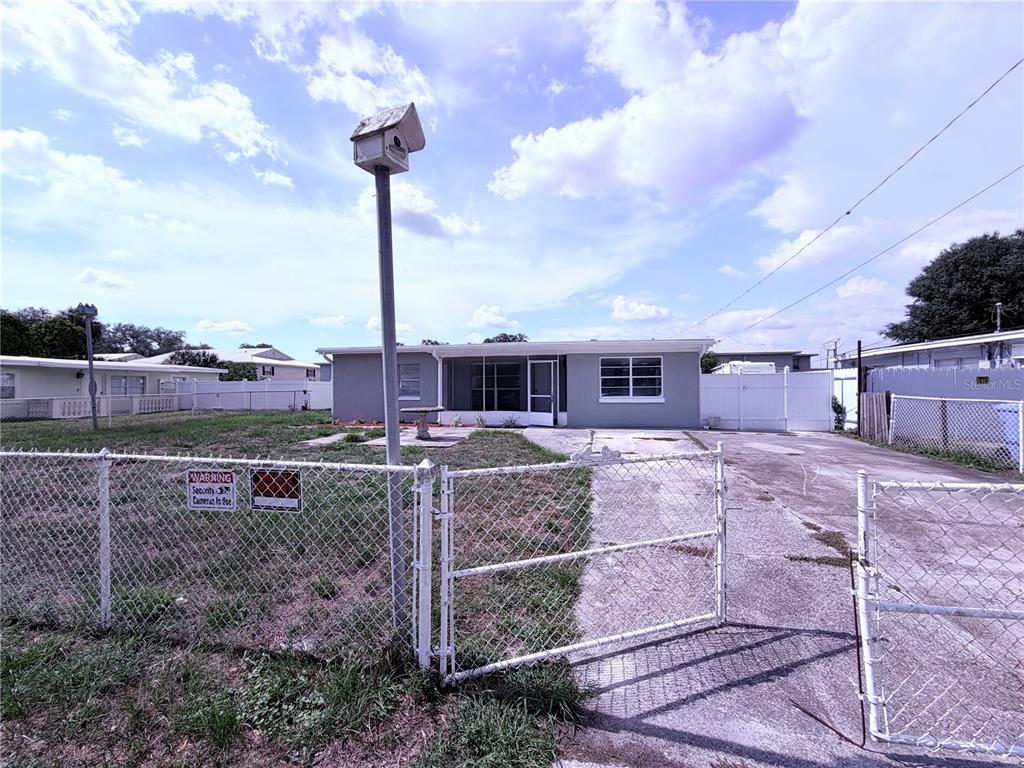 A single-story house with a chain-link fence, a birdhouse on a pole, and a driveway — 7710 CORAL VINE LANE, TAMPA, FL