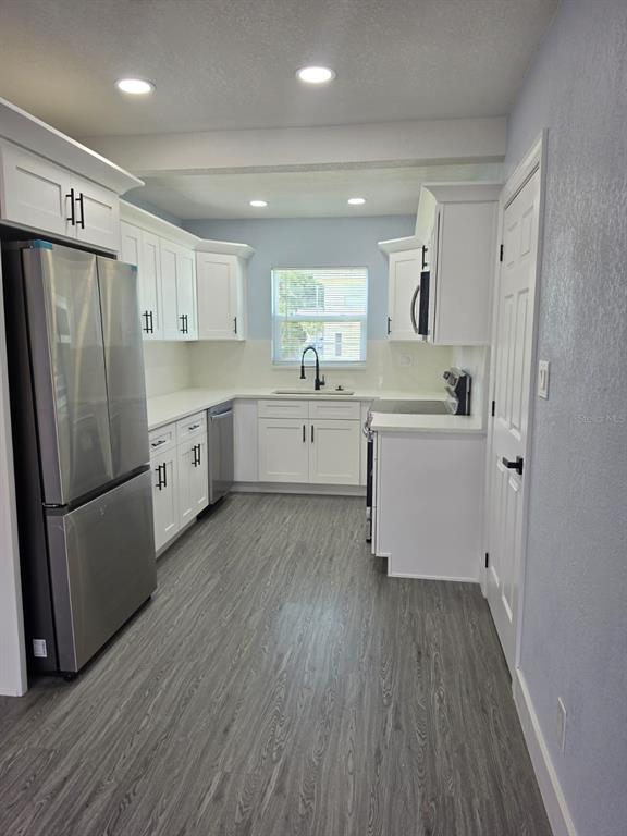 A kitchen features white cabinets, stainless steel appliances, and gray wood-look flooring — 7710 CORAL VINE LANE, TAMPA, FL