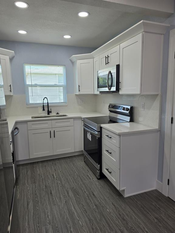 A kitchen features white cabinets, stainless steel appliances, quartz countertops, and gray wood-look flooring — 7710 CORAL VINE LANE, TAMPA, FL
