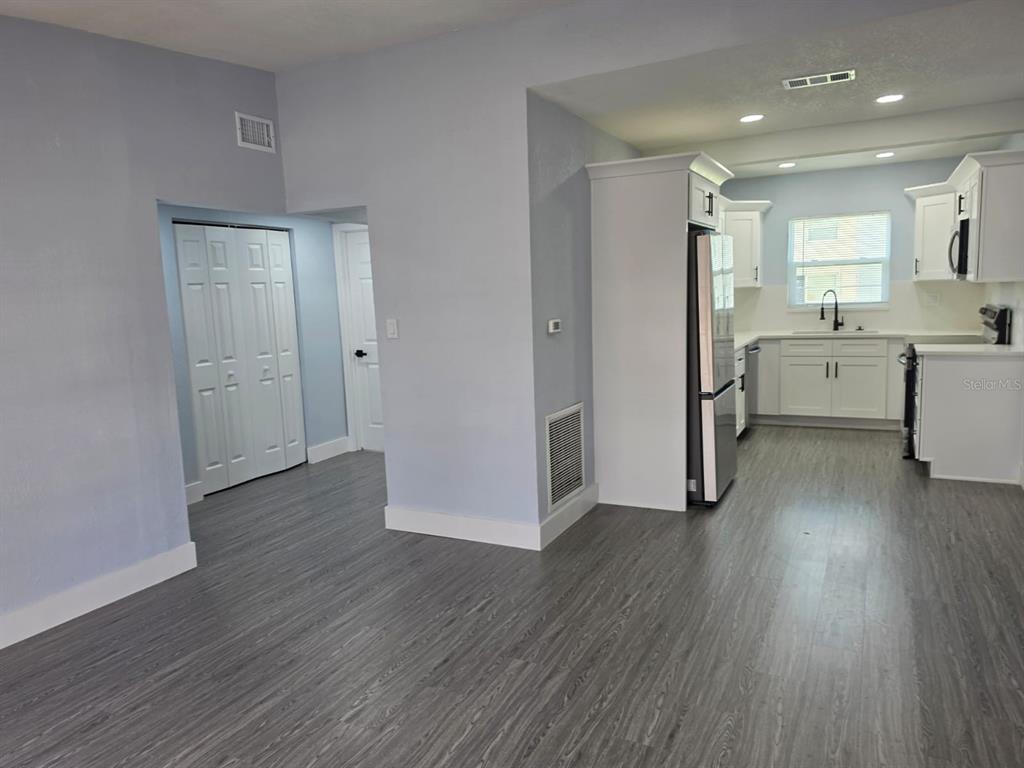 A kitchen with white cabinets and stainless steel appliances opens to a room with flooring — 7710 CORAL VINE LANE, TAMPA, FL