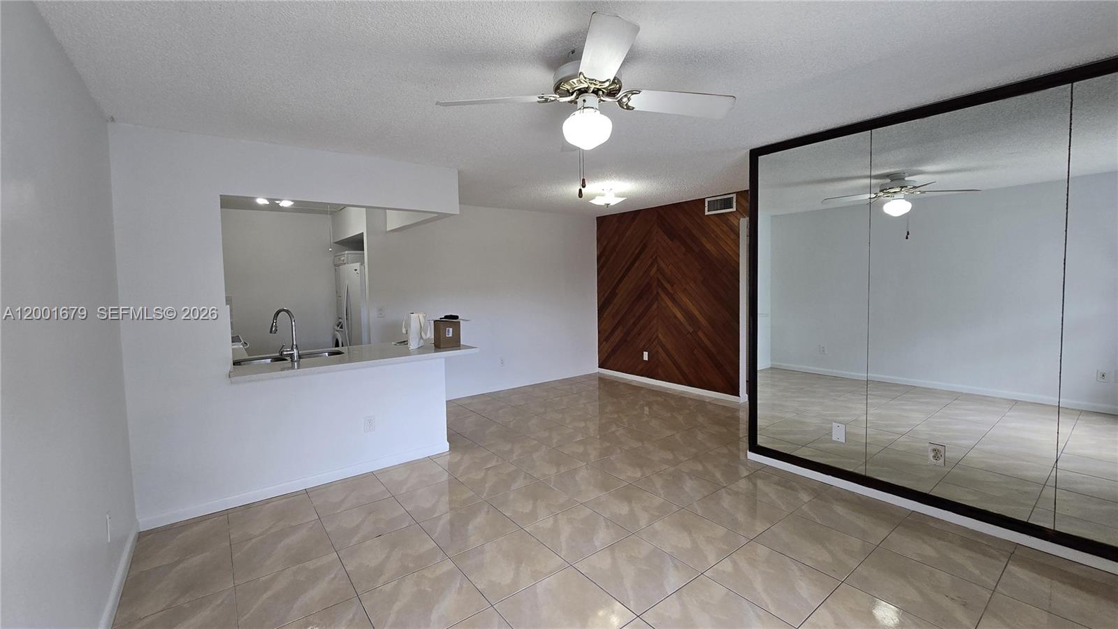 A living room features tile flooring, a wood-paneled accent wall, and a mirrored closet — 2605 W 67th Pl # 10, Hialeah FL 33016, HIALEAH, FL