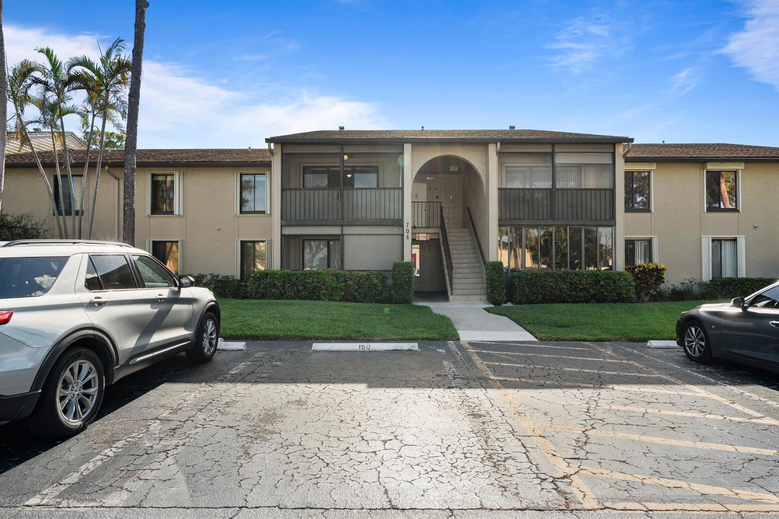 A two-story apartment building with a central staircase and parking spaces in the foreground — 706 Sunny Pine Way # E2, FL 33415, FL