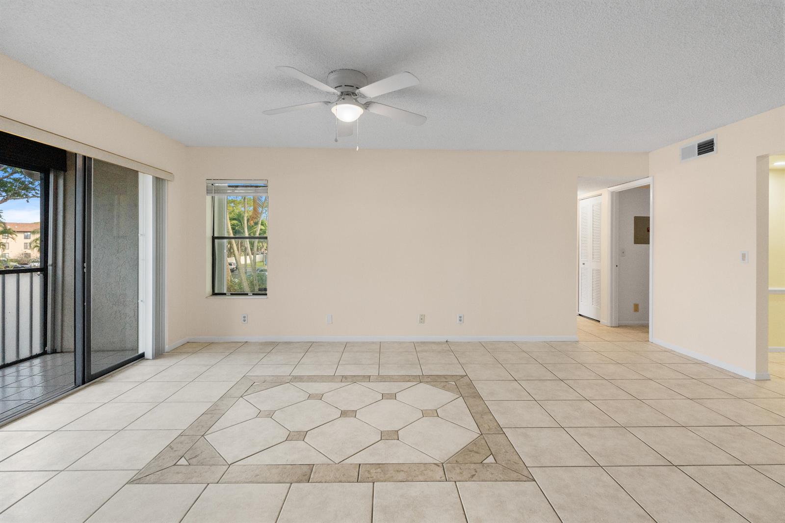 An empty living room features beige tile flooring, a ceiling fan, and a sliding glass door — 706 Sunny Pine Way # E2, FL 33415, FL