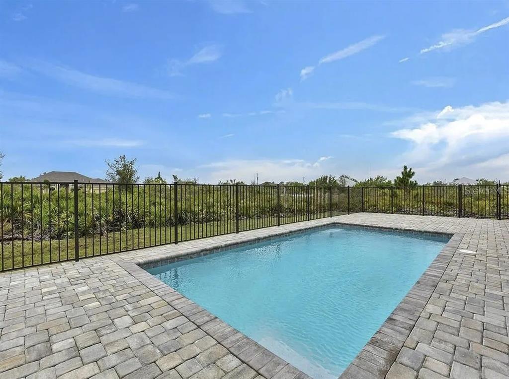 A rectangular swimming pool with a paver deck is enclosed by a black metal fence — 13575 ABUTILON LANE, PORT CHARLOTTE, FL