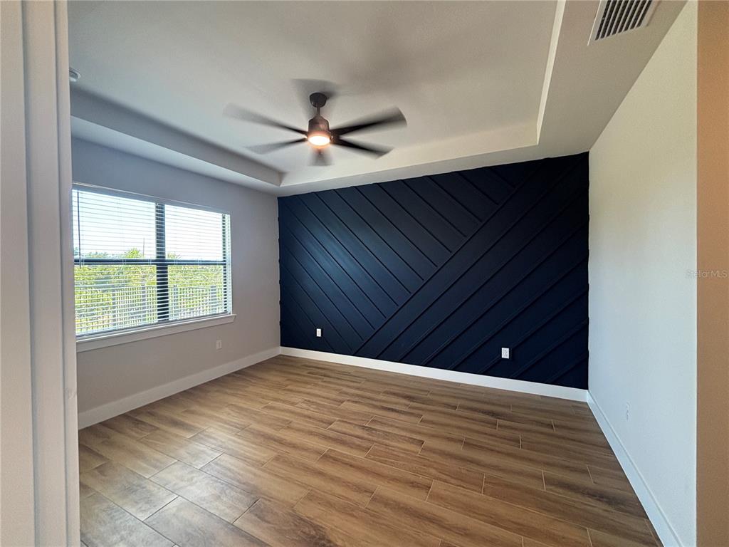 An empty bedroom features wood-look tile flooring, a tray ceiling, and a dark blue accent wall — 13575 ABUTILON LANE, PORT CHARLOTTE, FL
