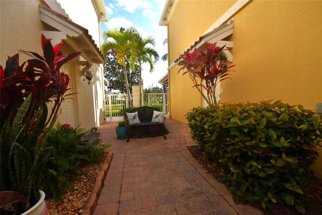 A brick walkway leads to a bench situated between two yellow stucco buildings with landscaping — 7624 BERGAMO AVENUE UNIT 4B, SARASOTA, FL