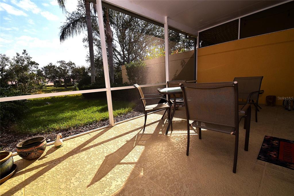 A screened-in patio features a dining set, concrete flooring, and a view of the lawn — 7624 BERGAMO AVENUE UNIT 4B, SARASOTA, FL