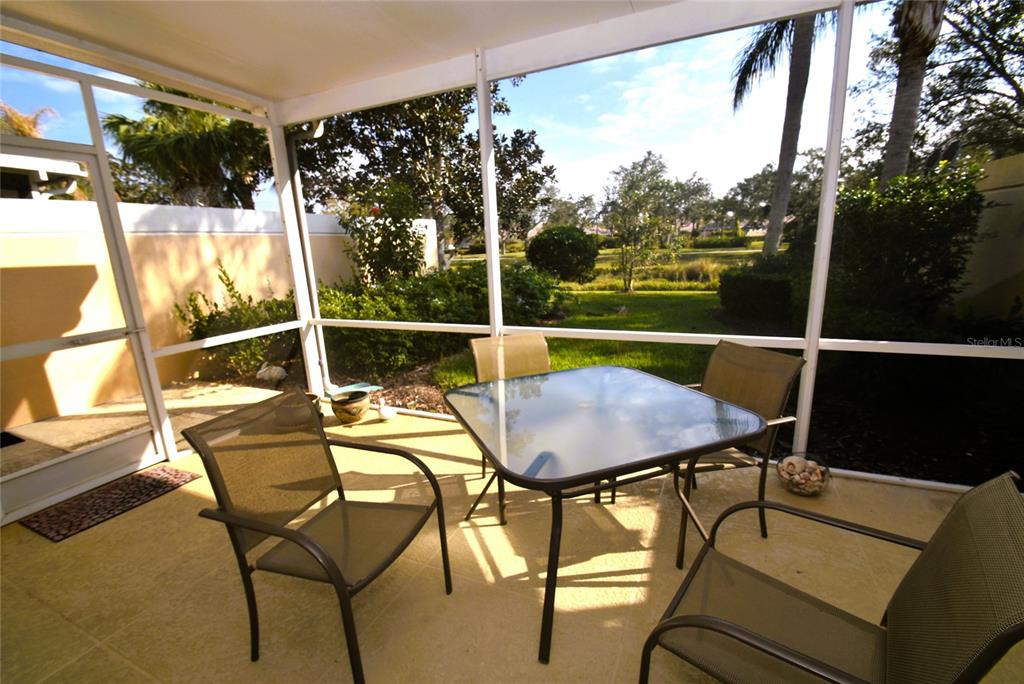 A screened-in patio features a glass-topped table with four chairs overlooking a grassy backyard — 7624 BERGAMO AVENUE UNIT 4B, SARASOTA, FL