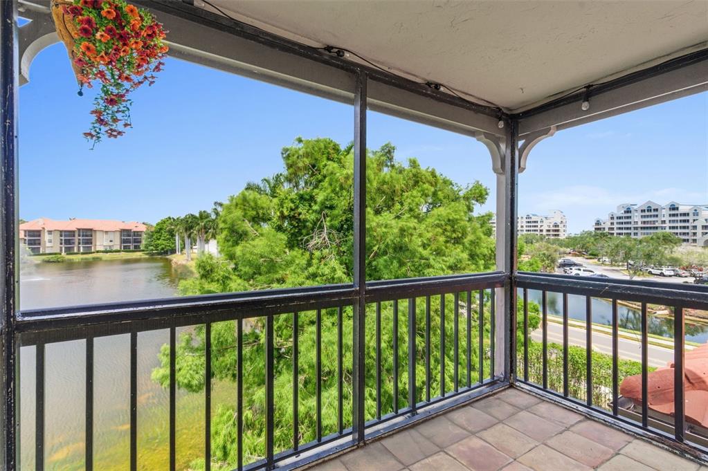 A screened-in balcony with tiled flooring overlooks a lake, trees, and nearby apartment buildings — 2400 FEATHER SOUND DRIVE UNIT 1136, CLEARWATER, FL